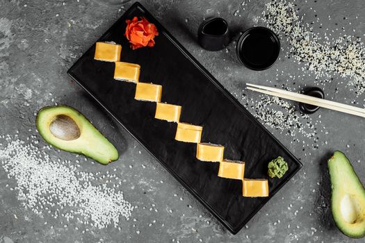 Traditional fresh japanese sushi rolls on a black stone Teka Kaji. Roll ingredients: cheese cheder, philadelphia cheese, cucumber, tuna chips, nori, rice.