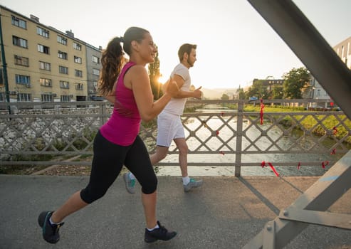 urban sports, healthy young couple jogging across the bridge in the city at sunny morning