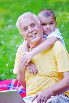 happy elderly senior grandfather and child in park using laptop computer