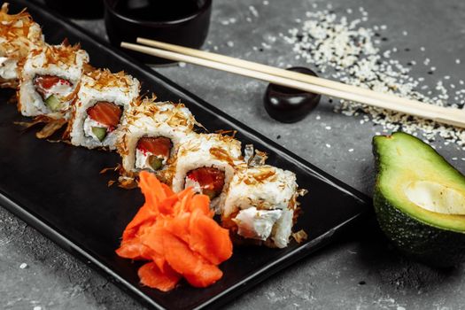 sushi rolls with cream cheese, fried salmon, tuna shavings or dried bonito, cucumber, nori. Chopsticks holding fresh katsuobushi roll in Japanese restaurant closeup.