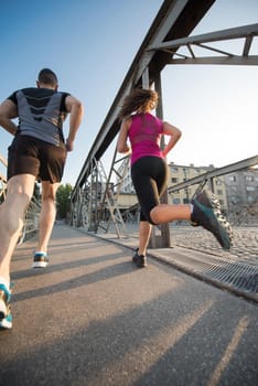 urban sports, healthy young couple jogging across the bridge in the city at sunny morning