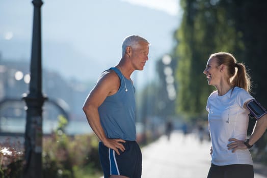 jogging couple check music playlist on phone and plan route before morning running workout  with sunrise in the city  and sun flare in background