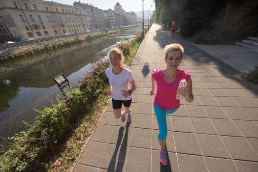 two middle aged female friends jogging have morning workout with sunrise in background