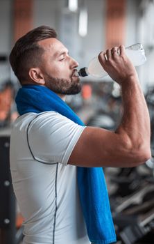 Young adult man drinking bottle of water on trreadmill in gym. concept of a healthy lifestyle