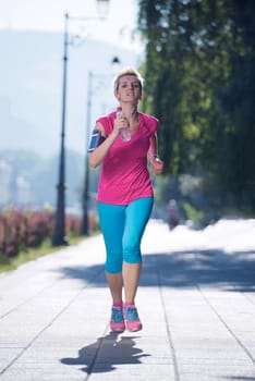 sporty woman running on sidewalk at early morning with city  sunrise scene in background