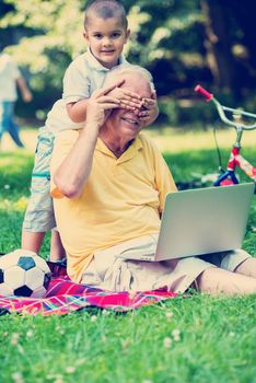 happy elderly senior grandfather and child in park using laptop computer