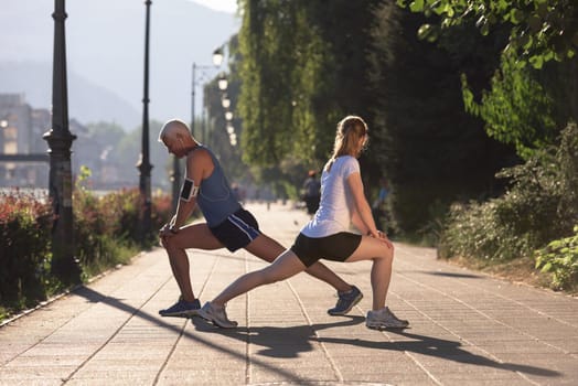 jogging couple warming up and stretching before morning running training workout  in the city with sunrise in background