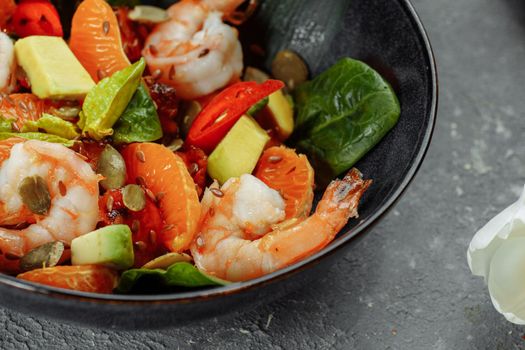 Shrimps salad with cherry tomatoes, cucumeber, avocado, lettuce and pomegranate on dish. Healthy seafood concept. Tasty grilled prawn shrimp and mix vegetable salad on black, top view.