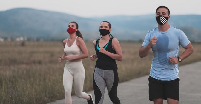 Three multiethnic women runners group wear face masks running keep social distance outdoor. Fit healthy diverse team wears sportswear jogging in park on nature sports track distancing for safety.