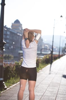 Fit blonde runner   woman warming up and stretching before morning jogging