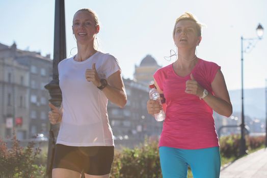 two middle aged female friends jogging have morning workout with sunrise in background