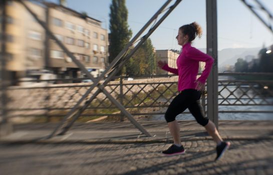 sporty woman running on sidewalk at early morning jogging with city  sunrise scene in background