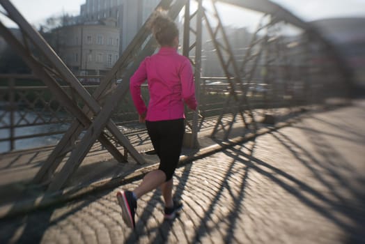 sporty woman running on sidewalk at early morning jogging with city  sunrise scene in background