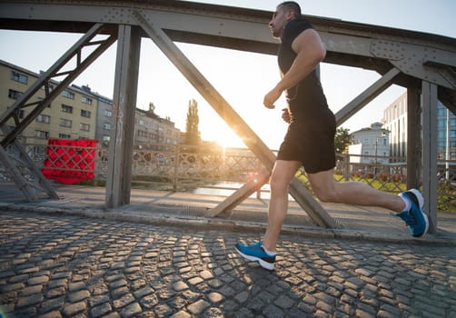 young sporty man jogging across the bridge at sunny morning in the city