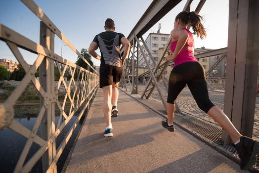 urban sports, healthy young couple jogging across the bridge in the city at sunny morning