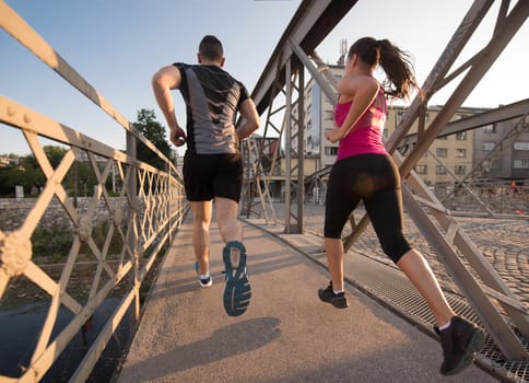 urban sports, healthy young couple jogging across the bridge in the city at sunny morning