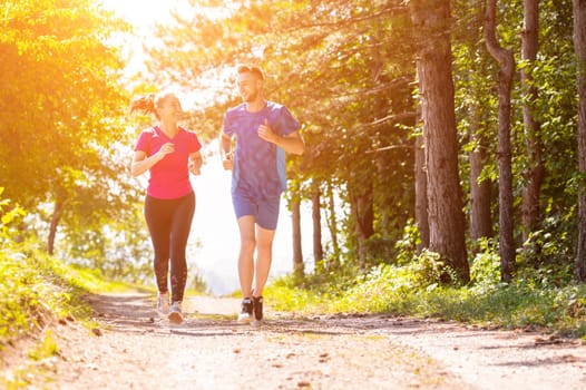 young happy couple enjoying in a healthy lifestyle while jogging on a country road through the beautiful sunny forest, exercise and fitness concept