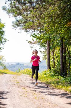 young happy woman enjoying in a healthy lifestyle while jogging on a country road through the beautiful sunny forest, exercise and fitness concept