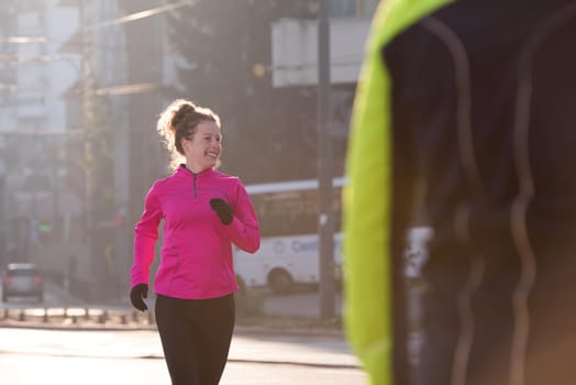 sporty woman running on sidewalk at early morning jogging with city  sunrise scene in background