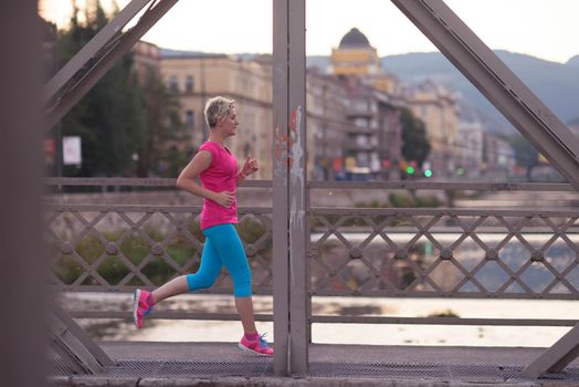 sporty woman running on sidewalk at early morning with city  sunrise scene in background