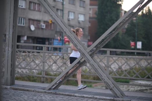 sporty woman running on sidewalk at early morning with city  sunrise scene in background