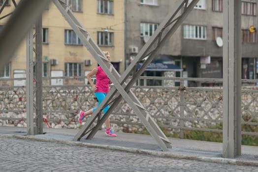 sporty woman running on sidewalk at early morning with city  sunrise scene in background