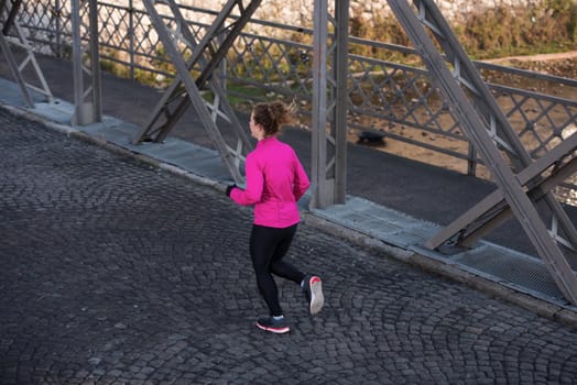 sporty woman running on sidewalk at early morning jogging with city  sunrise scene in background