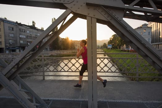 young sporty woman jogging across the bridge at sunny morning in the city