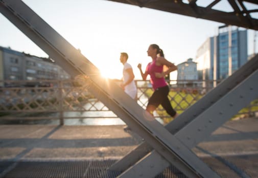 urban sports, healthy young couple jogging across the bridge in the city at sunny morning