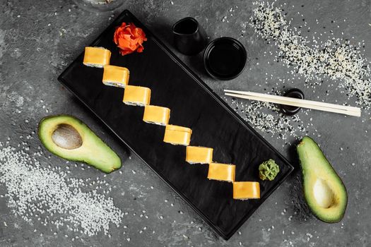 Traditional fresh japanese sushi rolls on a black stone Teka Kaji. Roll ingredients: cheese cheder, philadelphia cheese, cucumber, tuna chips, nori, rice.