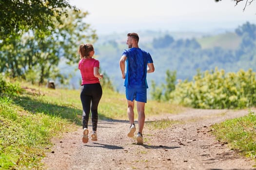 young happy couple enjoying in a healthy lifestyle while jogging on a country road through the beautiful sunny forest, exercise and fitness concept