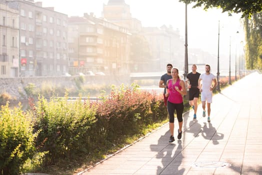 group of young sporty people jogging at sunny morning in the city