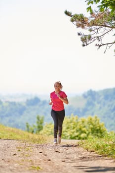 woman enjoying in a healthy lifestyle while jogging on a country road through the beautiful sunny forest, exercise and fitness concept