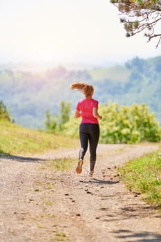 woman enjoying in a healthy lifestyle while jogging on a country road through the beautiful sunny forest, exercise and fitness concept