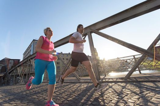 healthy mature couple jogging in the city  at early morning with sunrise in background