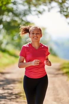woman enjoying in a healthy lifestyle while jogging on a country road through the beautiful sunny forest, exercise and fitness concept