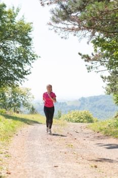 woman enjoying in a healthy lifestyle while jogging on a country road through the beautiful sunny forest, exercise and fitness concept