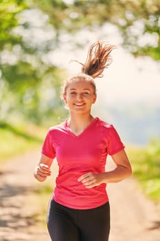 woman enjoying in a healthy lifestyle while jogging on a country road through the beautiful sunny forest, exercise and fitness concept