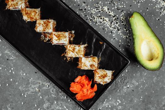 sushi rolls with cream cheese, fried salmon, tuna shavings or dried bonito, cucumber, nori. Chopsticks holding fresh katsuobushi roll in Japanese restaurant closeup.