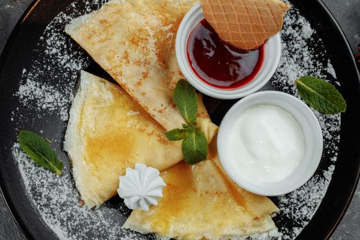 Pancakes with strawberries and creme black plate.