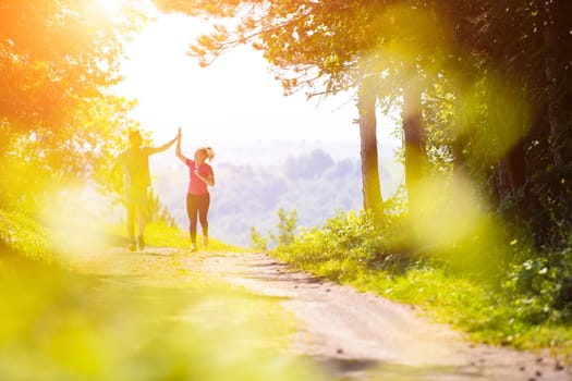 young happy couple enjoying in a healthy lifestyle giving high five to each other after jogging on a country road through the beautiful sunny forest, exercise and fitness concept