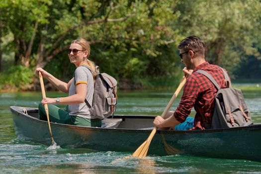 Couple adventurous explorer friends are canoeing in a wild river surrounded by the beautiful nature