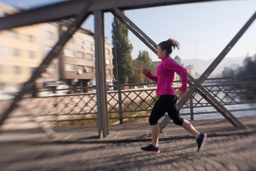 sporty woman running on sidewalk at early morning jogging with city  sunrise scene in background