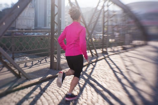 sporty woman running on sidewalk at early morning jogging with city  sunrise scene in background