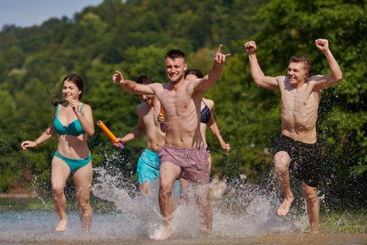 Summer joy group of happy friends having fun while running and splashing on river