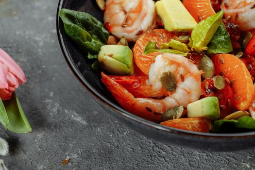 Shrimps salad with cherry tomatoes, cucumeber, avocado, lettuce and pomegranate on dish. Healthy seafood concept. Tasty grilled prawn shrimp and mix vegetable salad on black, top view.
