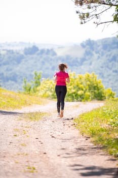 young happy woman enjoying in a healthy lifestyle while jogging on a country road through the beautiful sunny forest, exercise and fitness concept