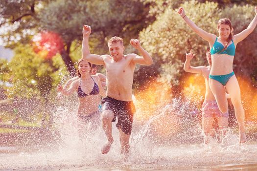 Summer joy group of happy friends having fun while running and splashing on river