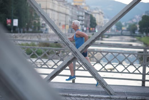 handsome senior man athlete jogging and  have morning workout with sunrise and city in background