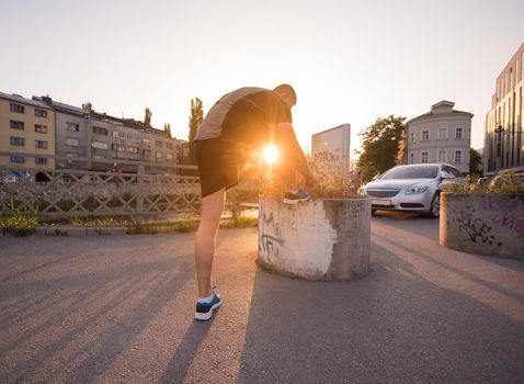 man tying running shoes laces getting ready to run on city at sunny morning